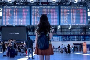 A passenger at a terminus, staring at wide variety of options in front of her on bulletin boards, trying to decide the path fourth.